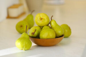 A wooden bowl full of green pears on a white countertop.