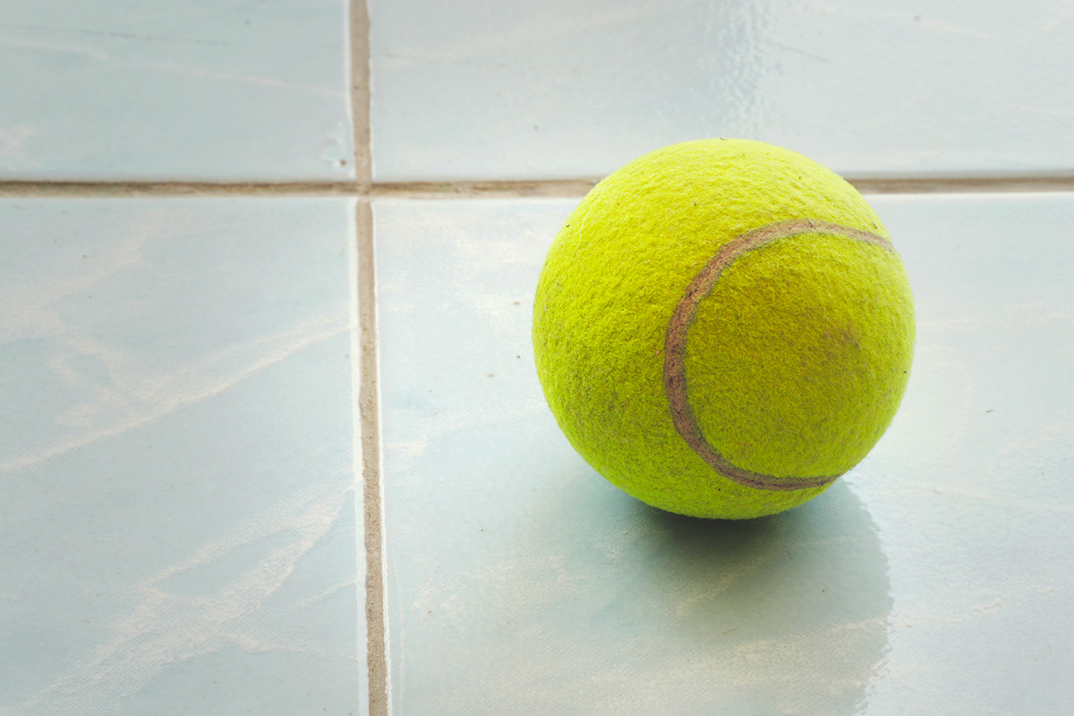 A bright yellow tennis ball on a light blue tile floor.