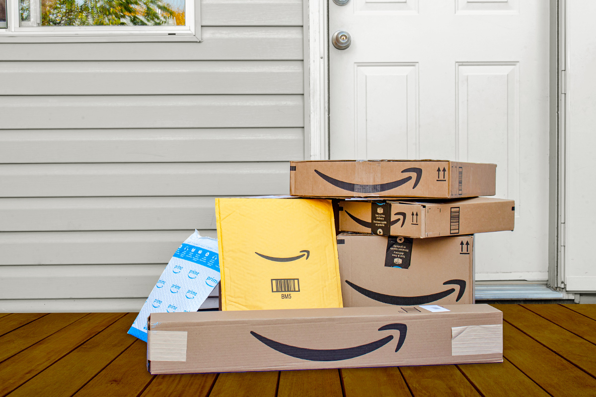 A stack of Amazon packages, including boxes and envelopes, in front of an exterior door.