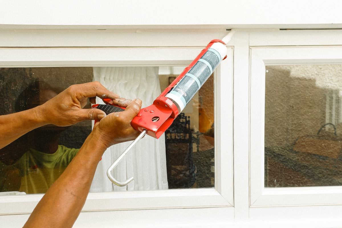 Anonymous person applying caulk to the outside of a window.