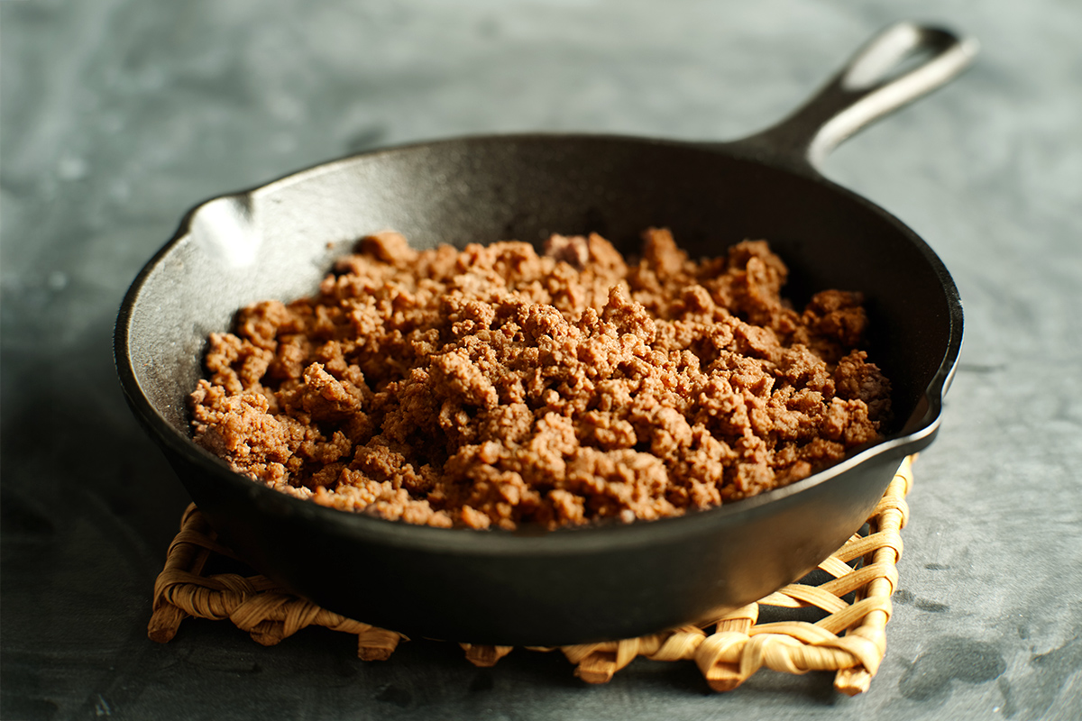 Perfectly browned ground beef in a cast iron skillet. The skillet is resting on a trivet on a stone countertop.