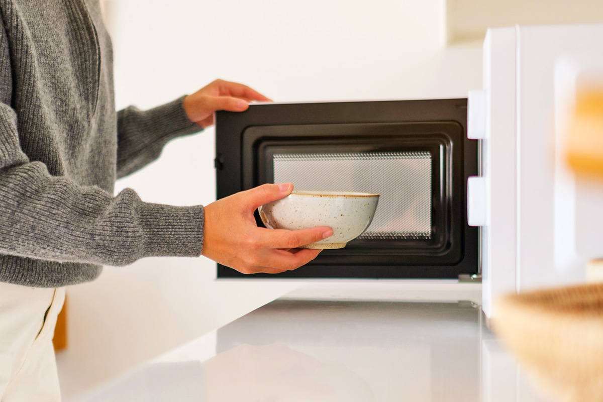 Anonymous person placing a ceramic bowl into a microwave with the door open.