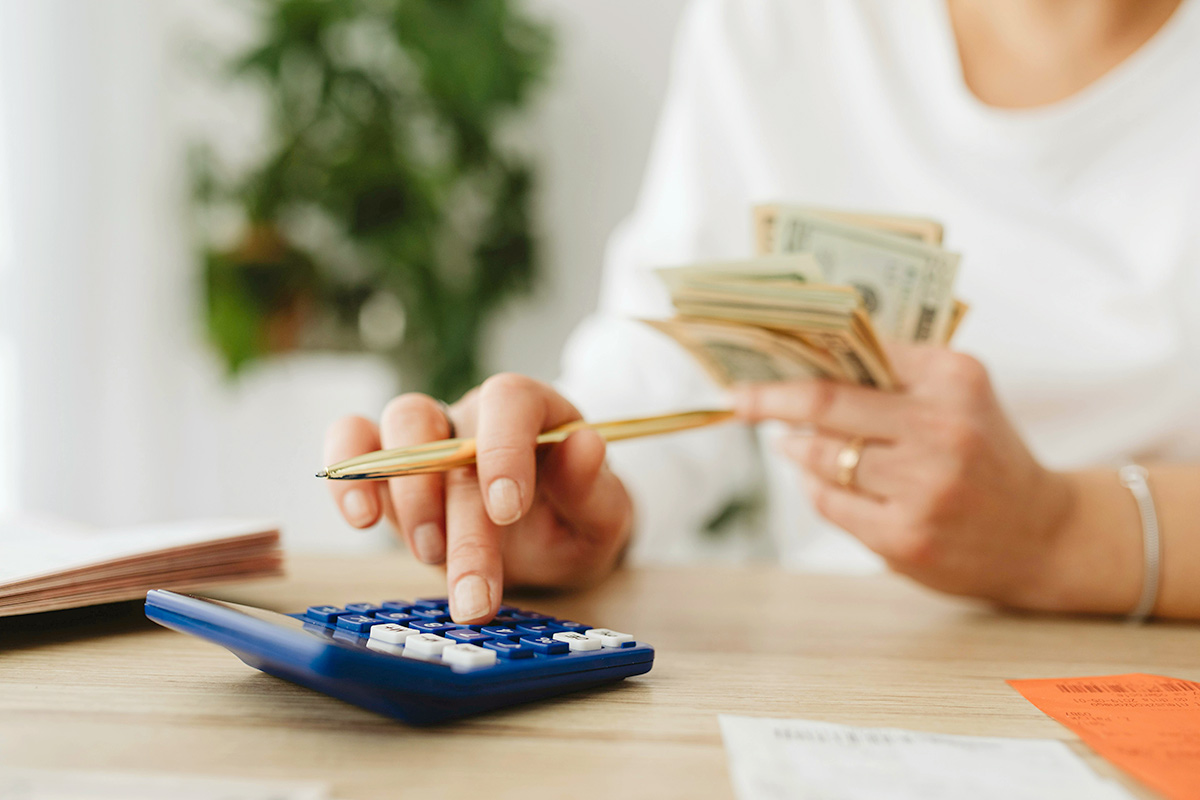 Anonymous person holding a wad of cash in one hand and using a calculator with the other.