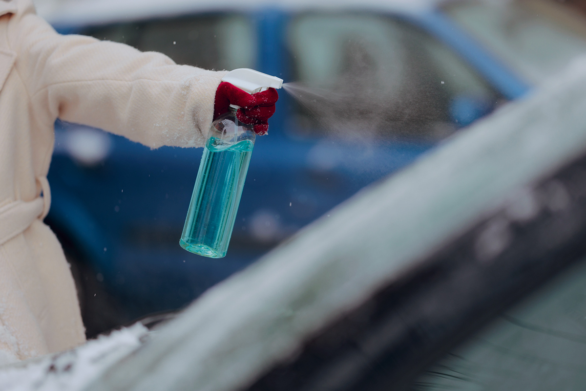 Spraying de-icer spray on car windshield