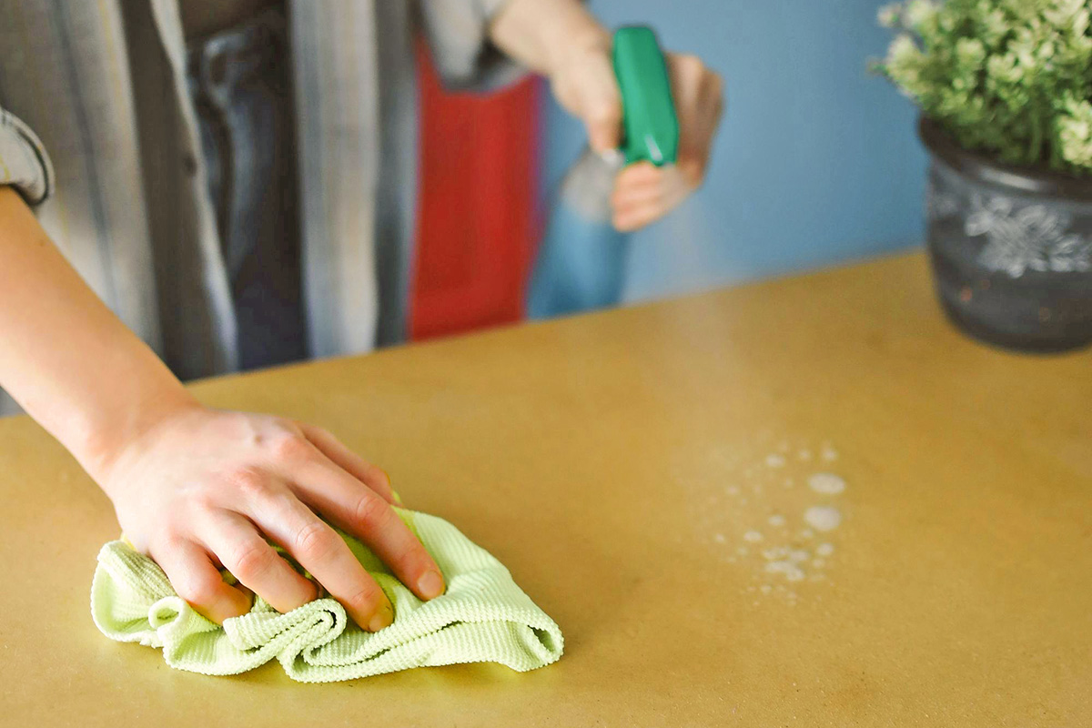 A person cleaning a table with disinfectant spray