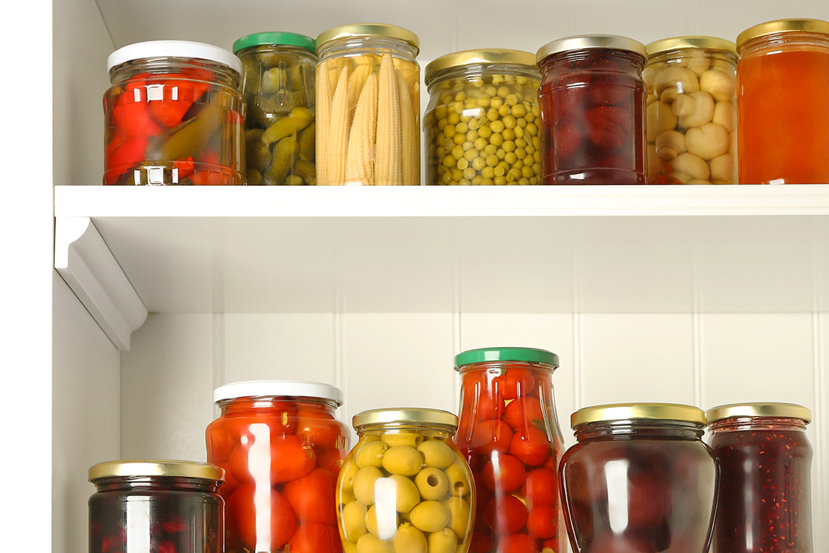 Jars of pickled fruits and vegetables on white wooden shelves in a pantry