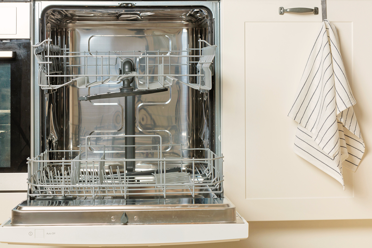 An open, empty dishwasher in a kitchen with off-white cabinetry.