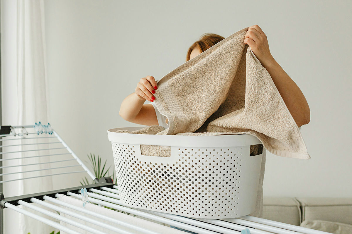 An anonymous woman grabbing a towel out of a laundry basket that's sitting on a drying rack.