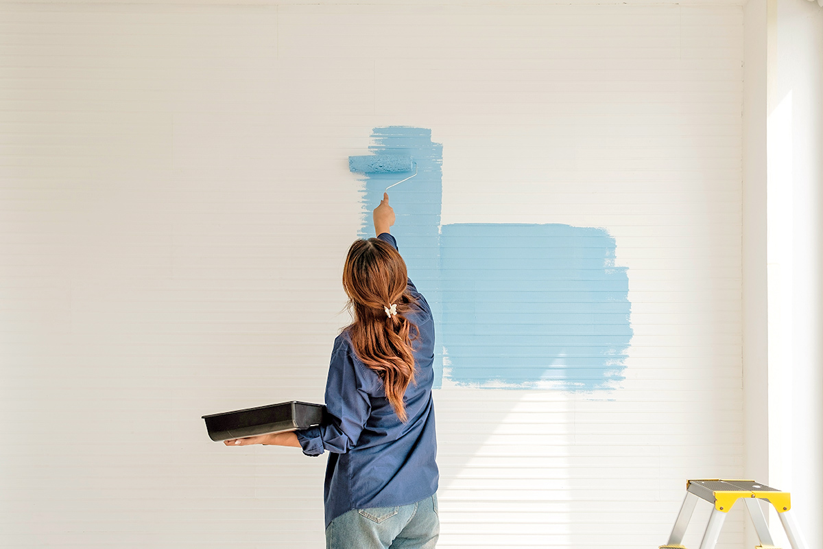 Anonymous woman rolling light blue paint onto a white slatted wall.