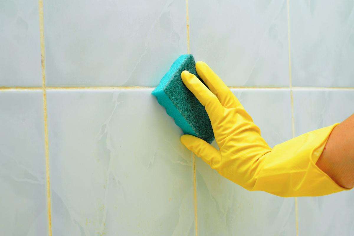 Anonymous person cleaning grout on a tile wall with a sponge.
