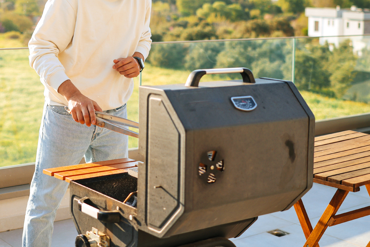 Anonymous man flipping food on an open grill with a pair of tongs.