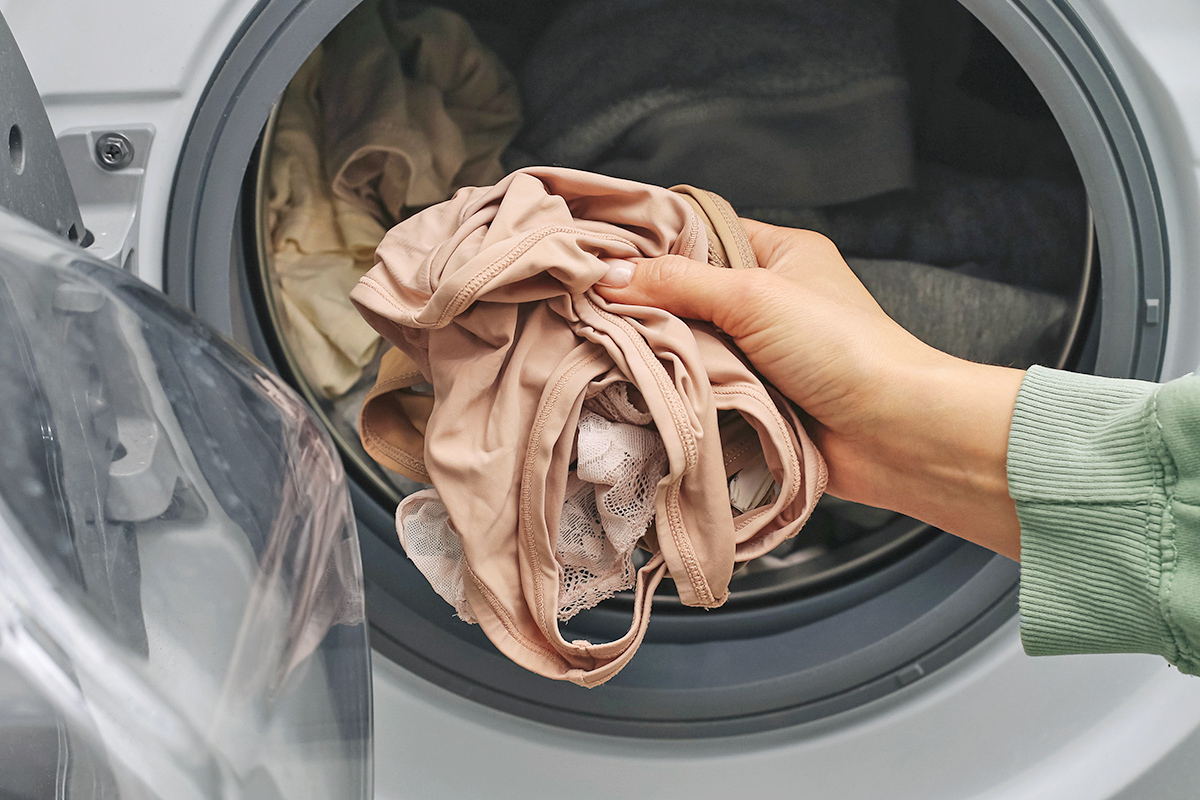 Anonymous person placing nude-colored underwear into a washing machine.