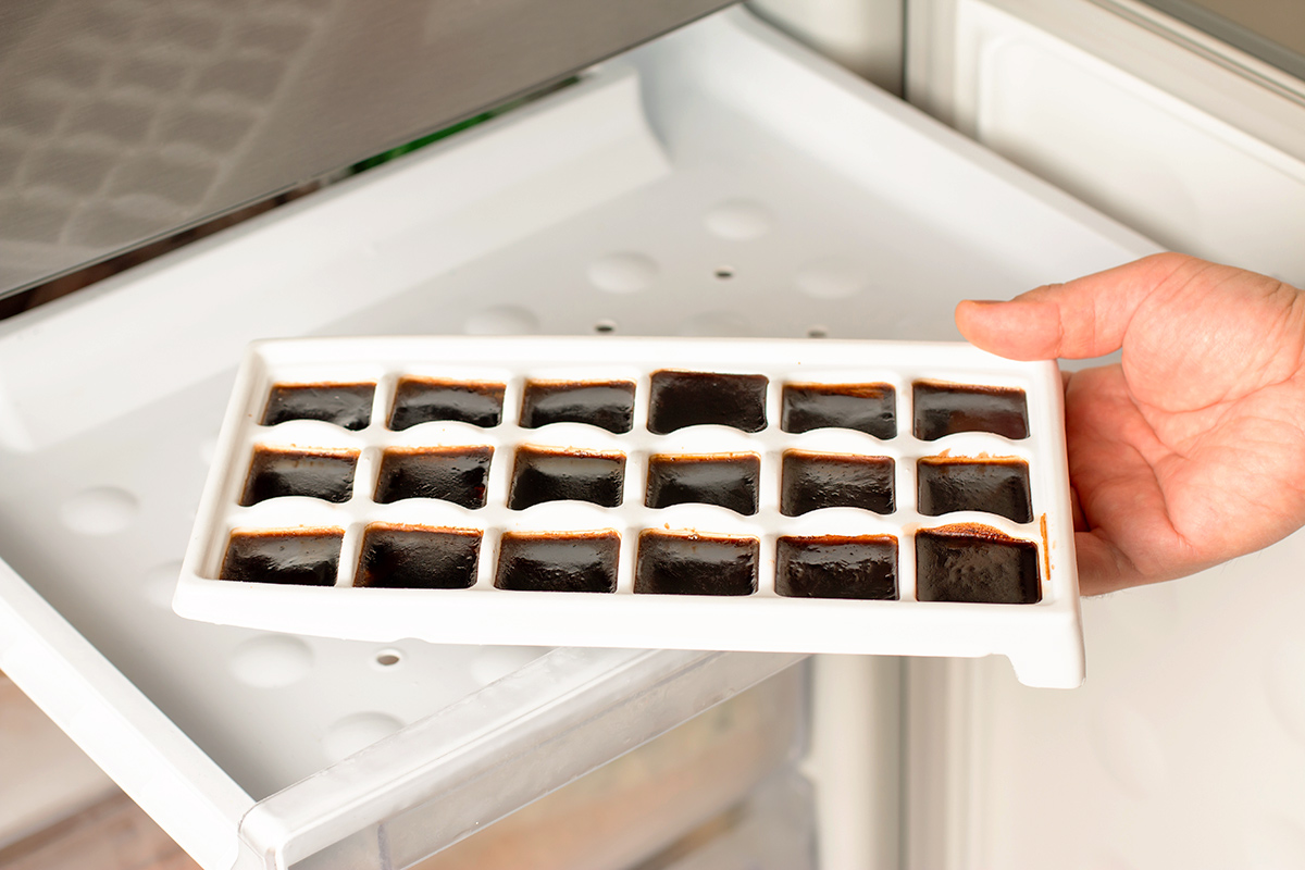 An anonymous person removing an ice cube tray filled with frozen coffee from the freezer.
