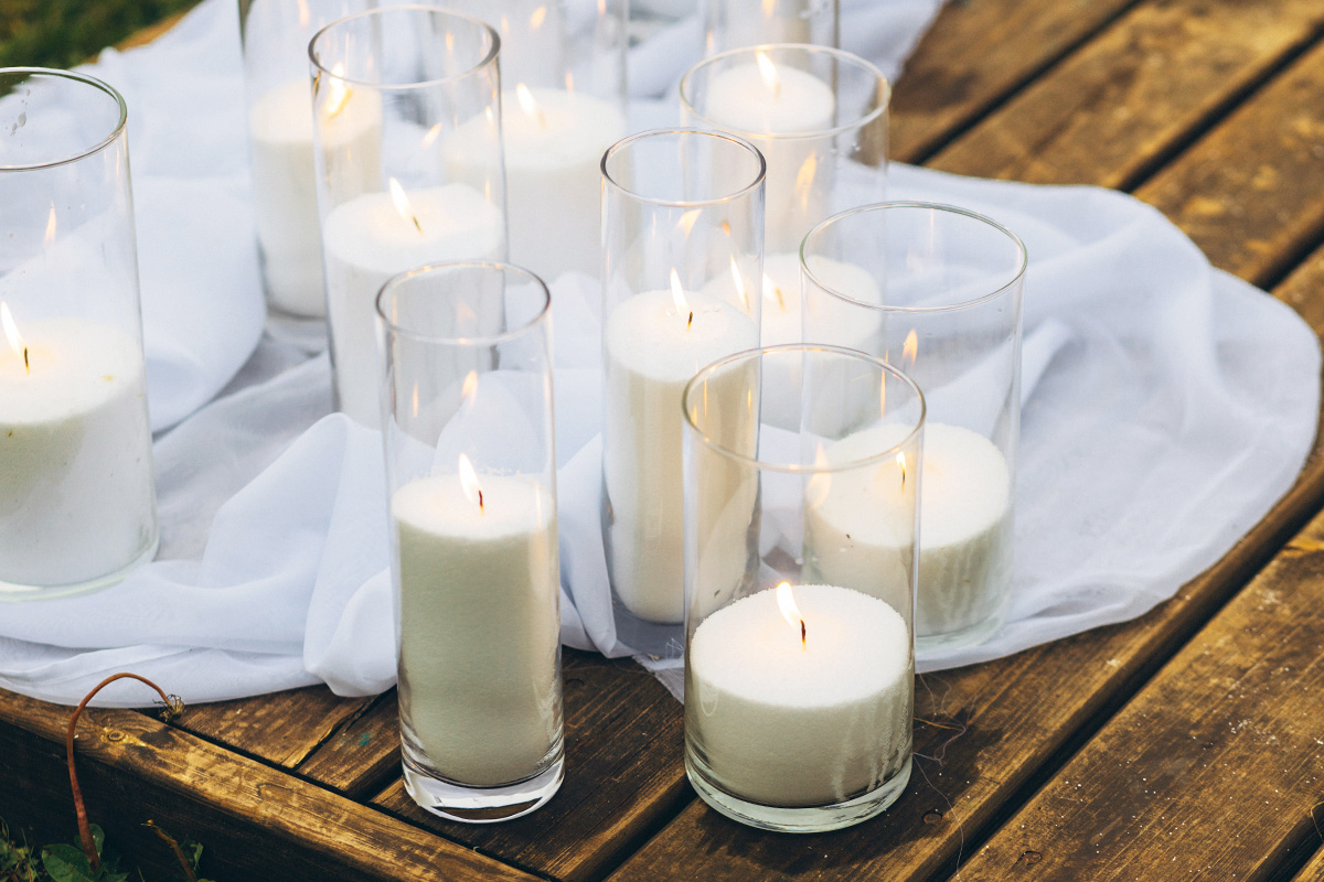 A cluster of pillar candles in clear glass hurricanes on a wood table.