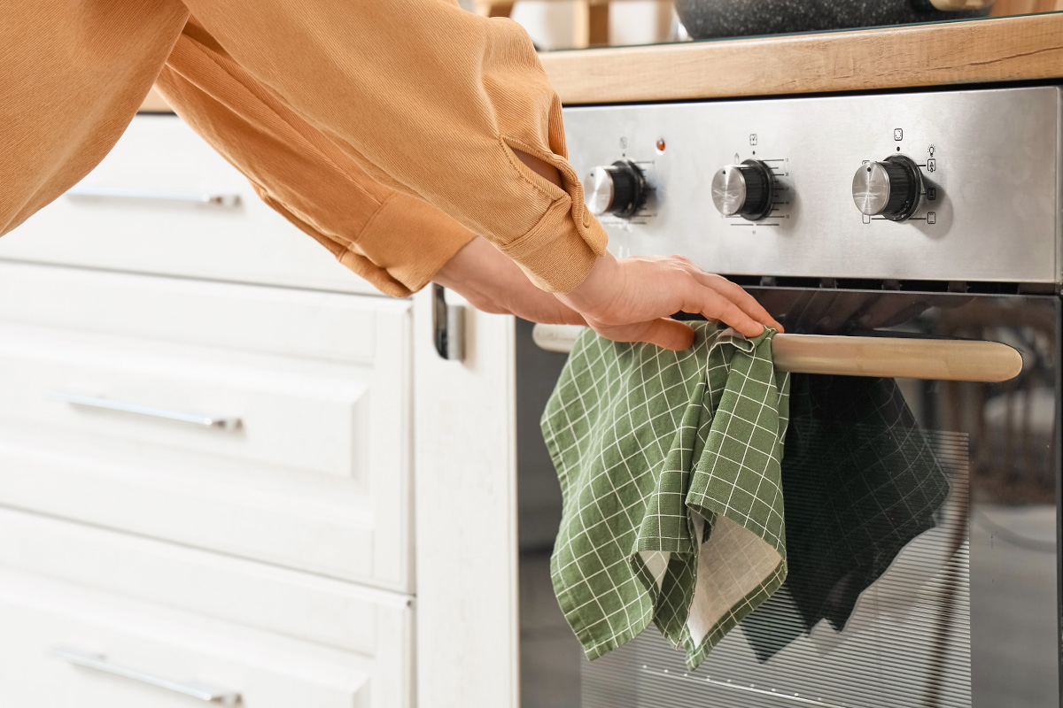 Anonymous person with both hands on an oven door handle. There's also a green tea towel hanging from the handle.